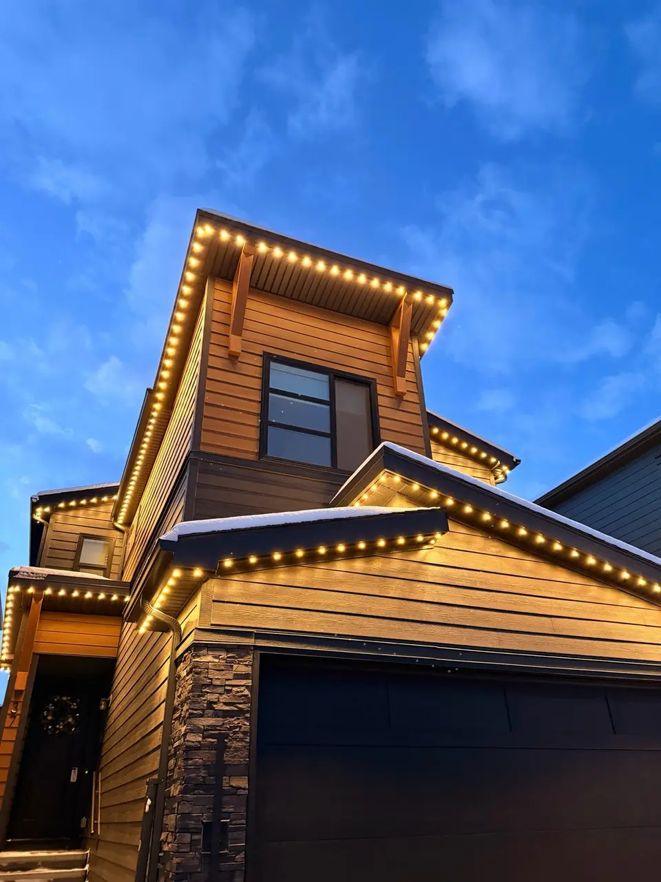 Warm white permanent accent lighting on cedar-tone Calgary home at blue hour