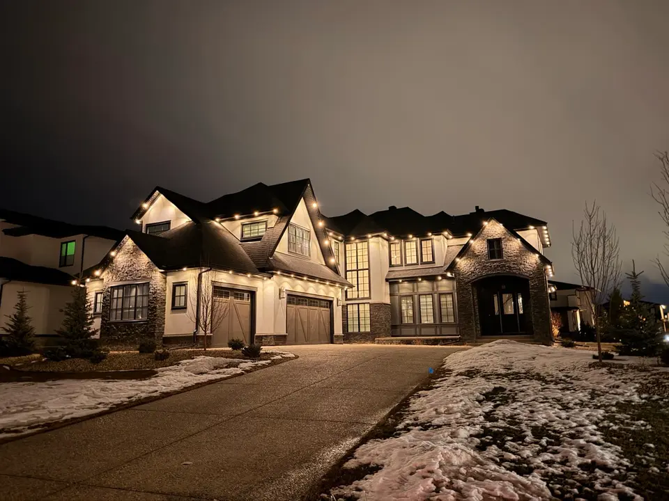 Snow-dusted Calgary estate street with warm white permanent lighting at dusk
